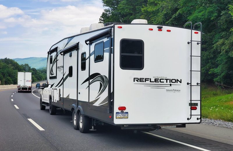 A pickup towing a large travel trailer on a tree-lined highway